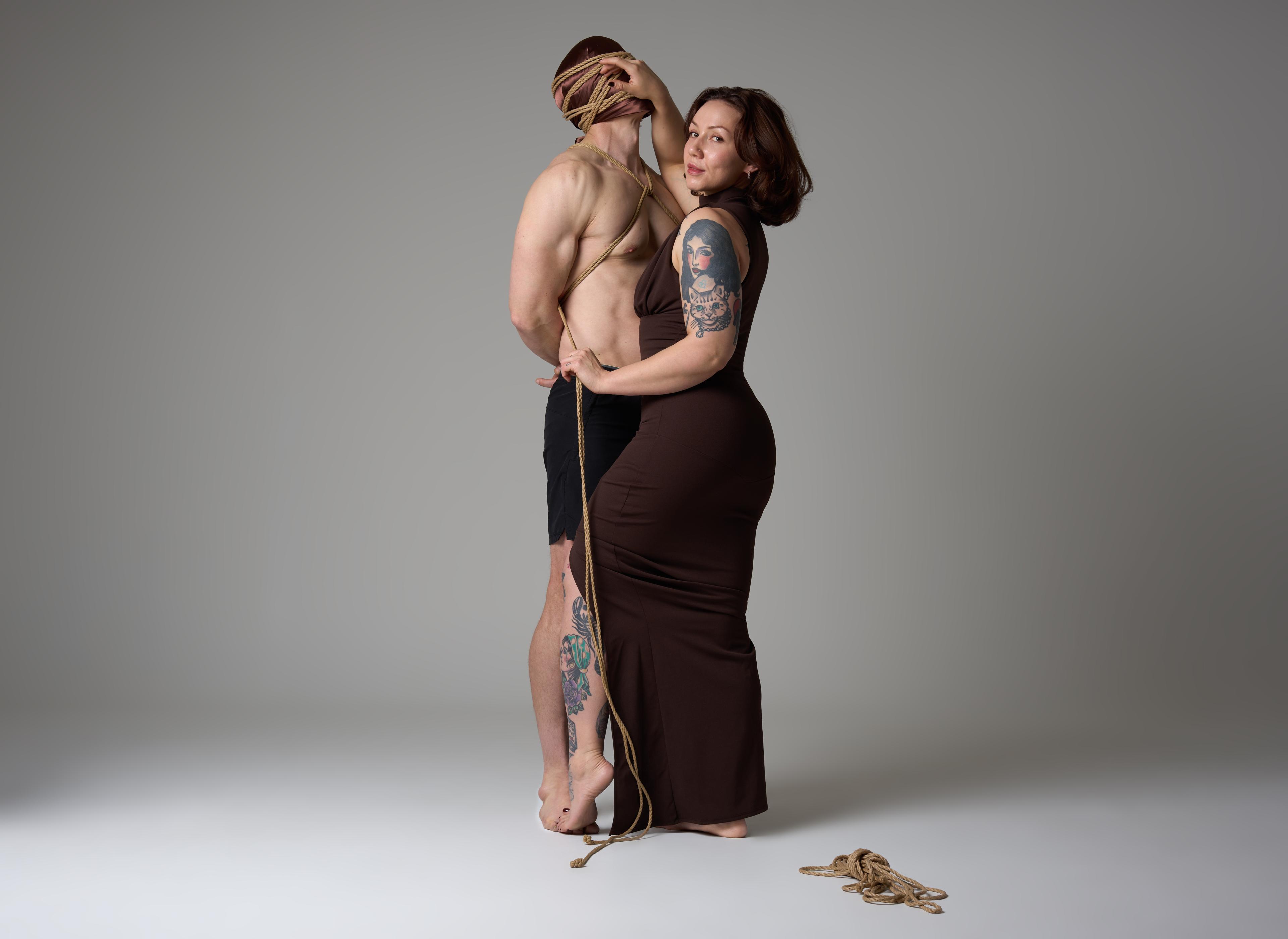 Sophia Rose tying a standing partner, their face wrapped in jute rope